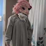 A person in a pink lion costume standing in front of a mirror at Carlie's Art Gallery.